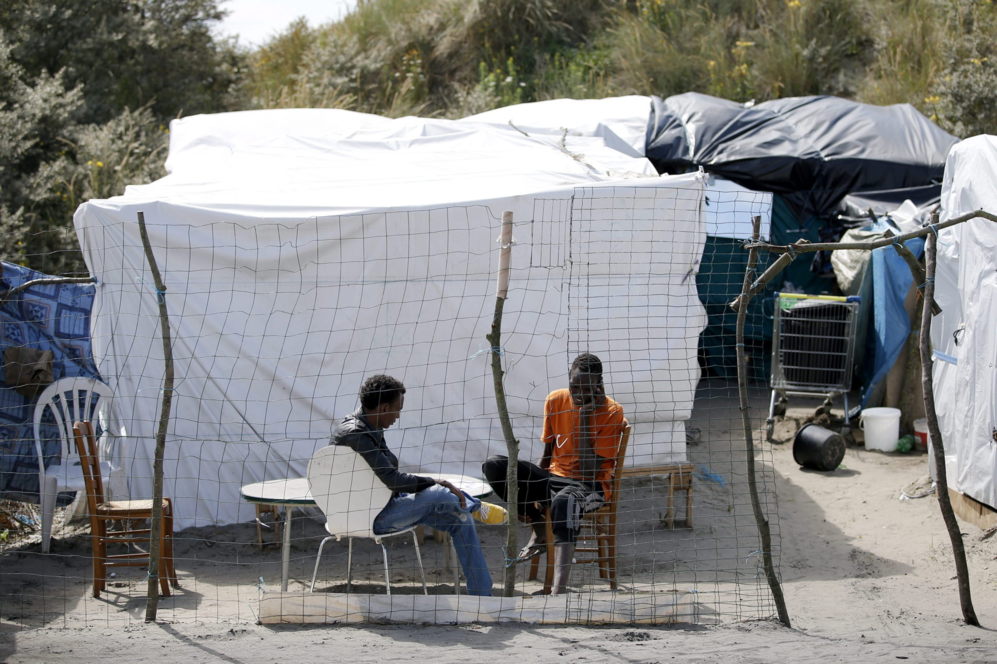 Dos inmigrantes descansan en el campamento improvisado mientras...