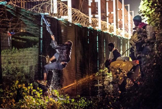 Un inmigrante sube por una valla de seguridad de la terminal del...