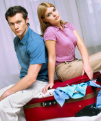 Una pareja sentada sobre una maleta sin cerrar