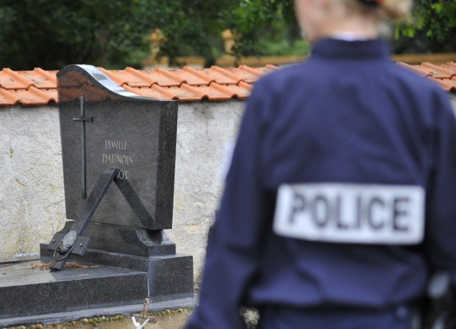 Un polica frente a una tumba con una cruz colocada al revs, en un...