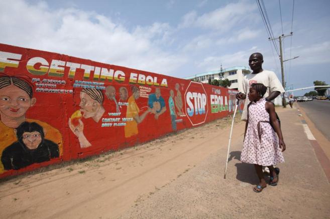 Una niña camina con su padre ciego delante de un mural que advierte...