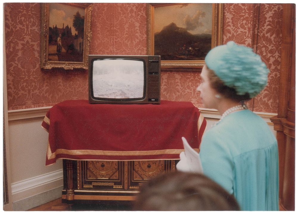 La reina Isabel II, ante un televisor donde puede verse a la...