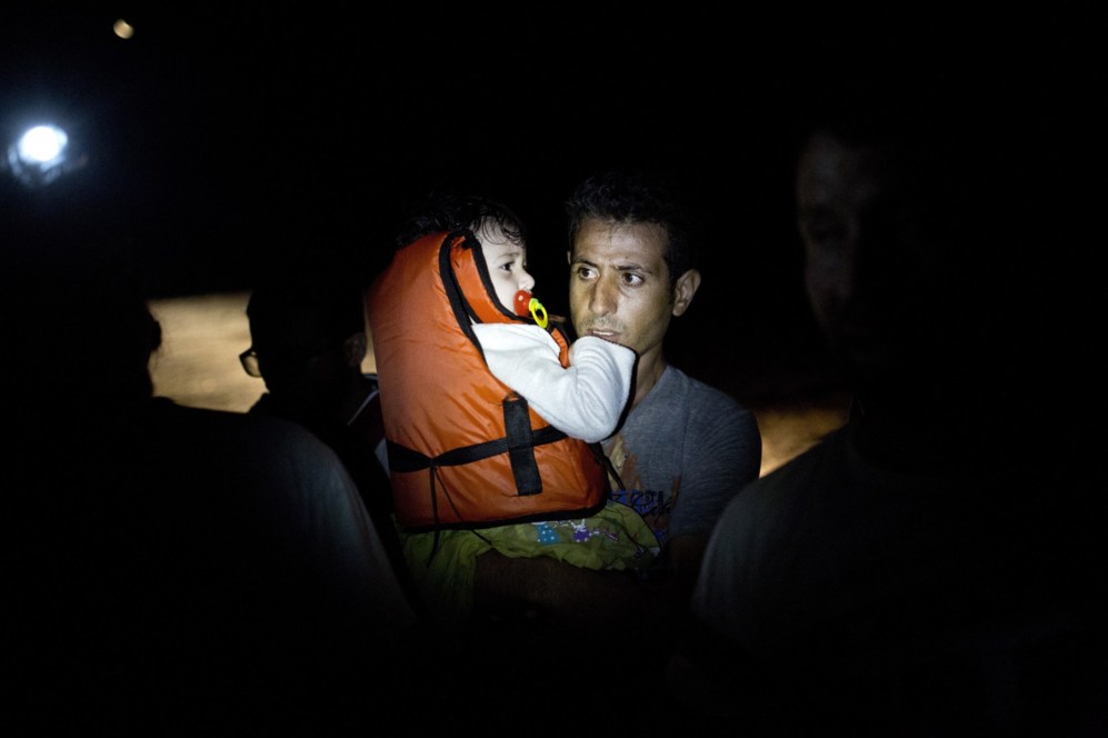 Un hombre sale de una barca inflable con su hijo en brazos tras llegar...
