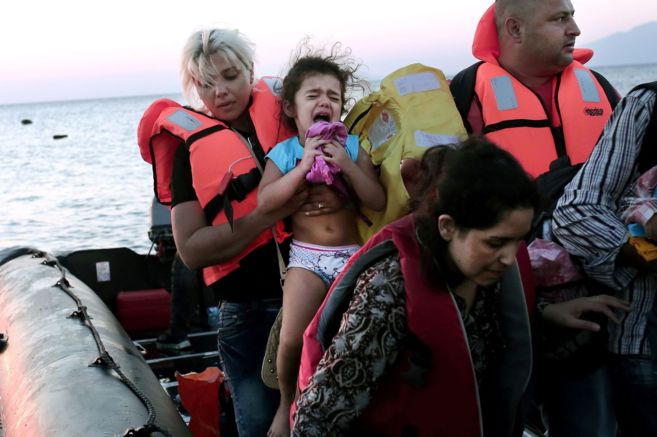 Un grupo de inmigrantes sale del barco inflable que les ha llevado...