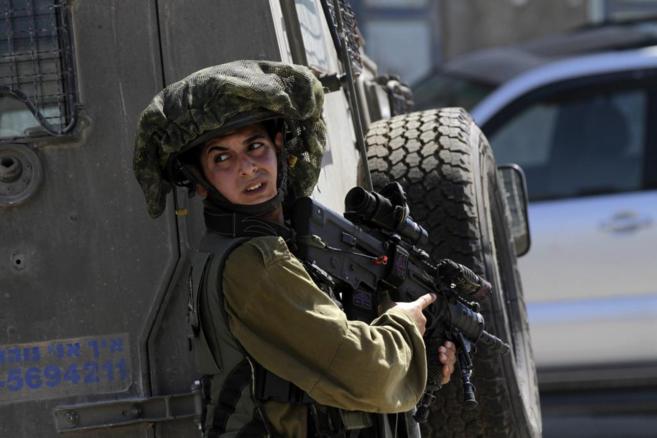 Un soldado israelí vigila a un grupo de palestinos que bloquean una...