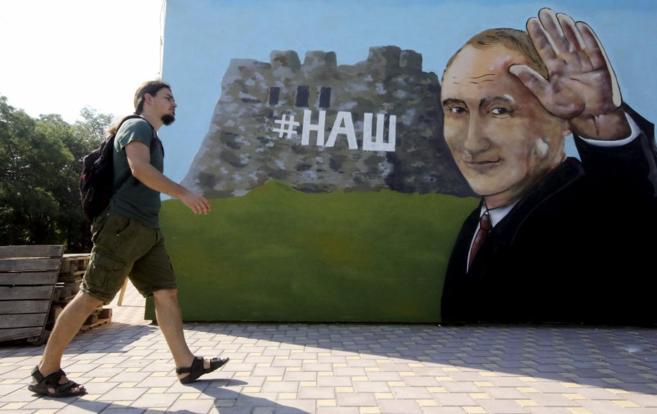 Un hombre pasa junto a un gran mural que da la bienvenida a Putin en...