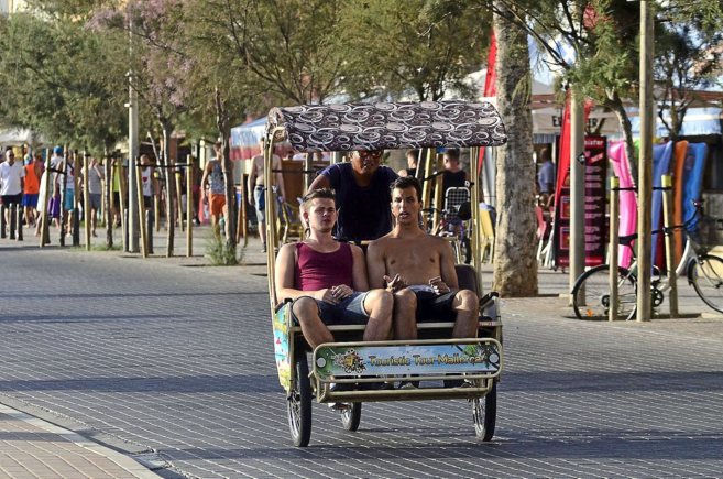 Un bicitaxi traslada a dos turistas en la Playa de Palma.