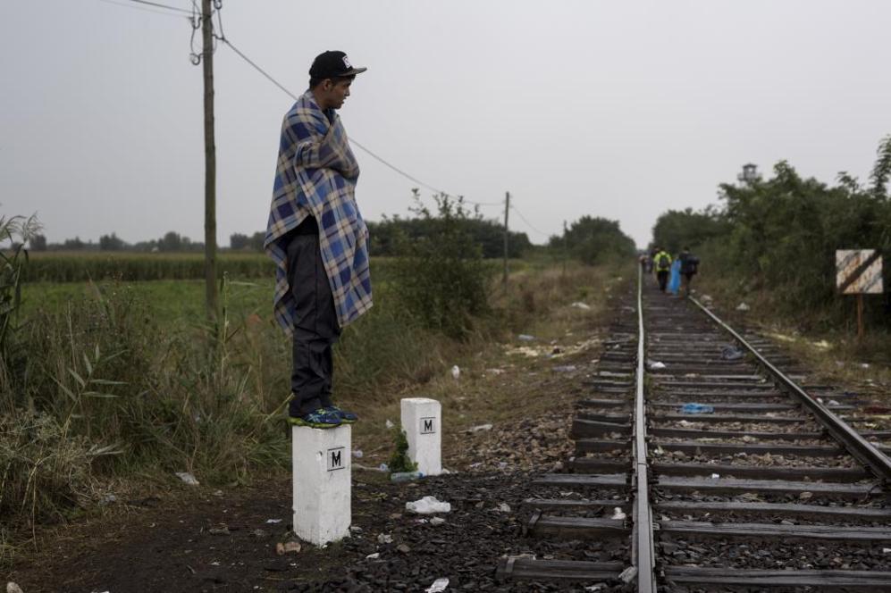 Un inmigrante sobre un poste, junto a las vas de tren que cruzan de...