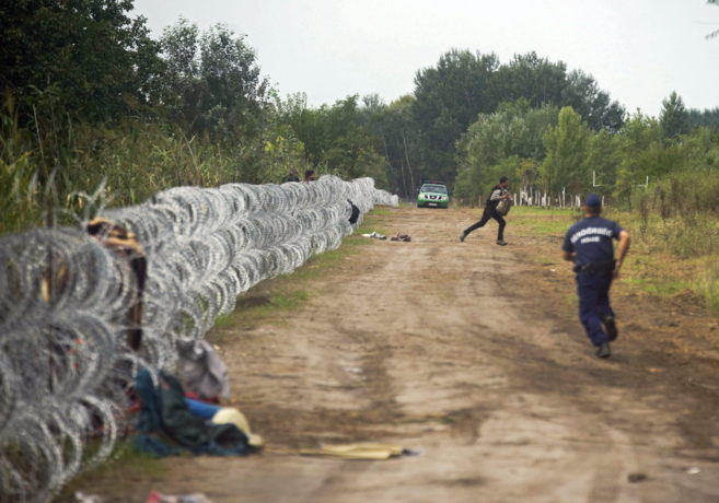 Un policía persigue a un inmigrante que cruzó la valla húngara, en...