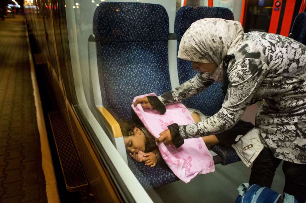 Una madre refugiada cubre a su hijo que duerme en un tren que viaja de...