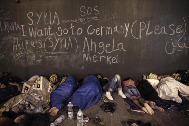 Varios refugiados duermen bajo un muro que reza: "Por favor,...