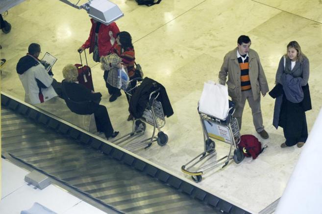 Pasajeros esperan para recoger sus maletas junto a una cinta...