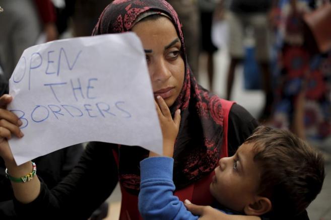Una mujer con su hijo en brazos sostiene un cartel con el lema:...