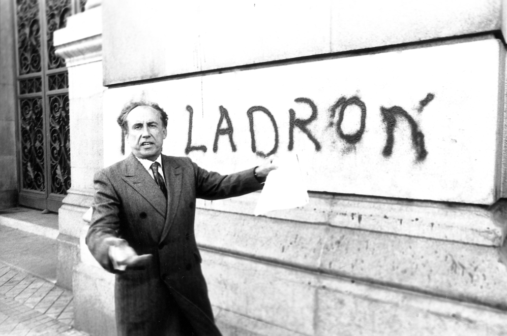 El ex presidente de Rumasa junto a una pintada en la calle que dice...
