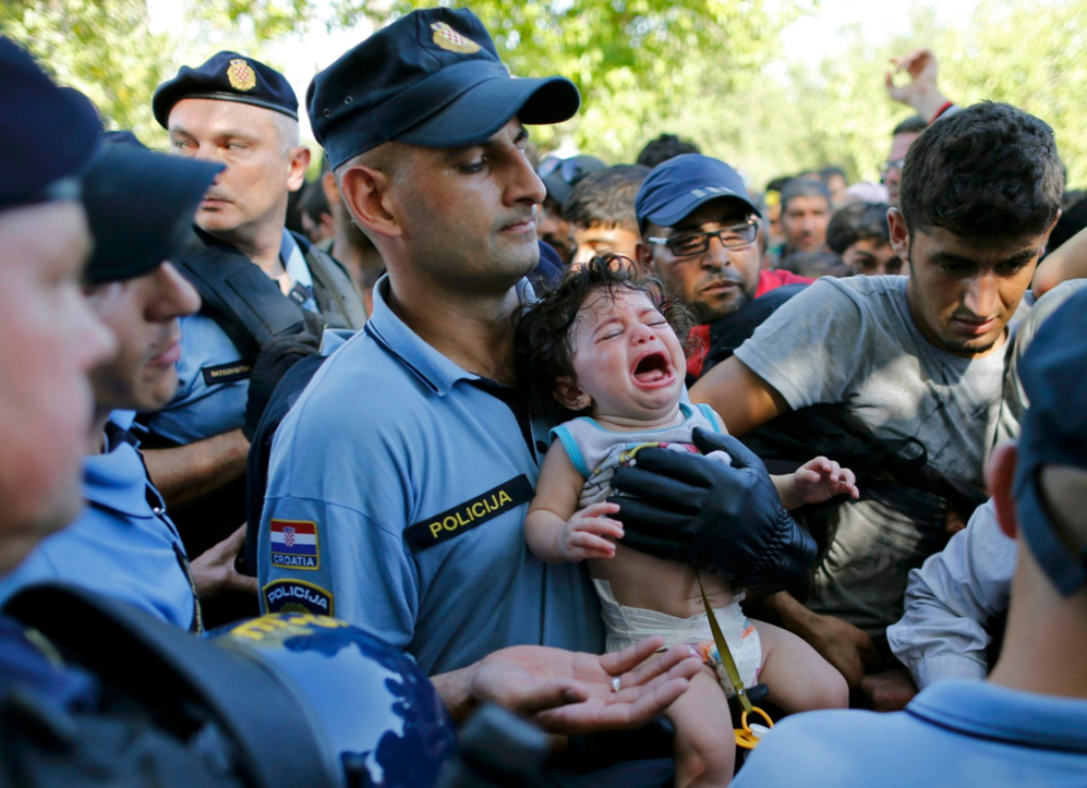 Un policía sostiene un bebé, que llora entre cientos de personas...