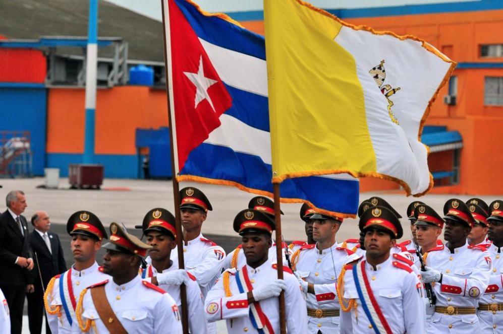 Soldados sostienen las banderas cubana y del Vaticano para rendir...