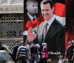 Sirios pasean por una calle en la que se han desplegado carteles con...