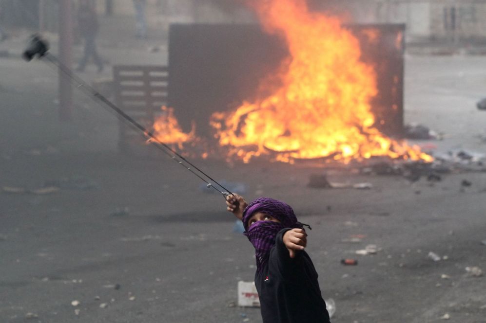Un joven palestino lanza una piedra contra las fuerzas de seguridad...