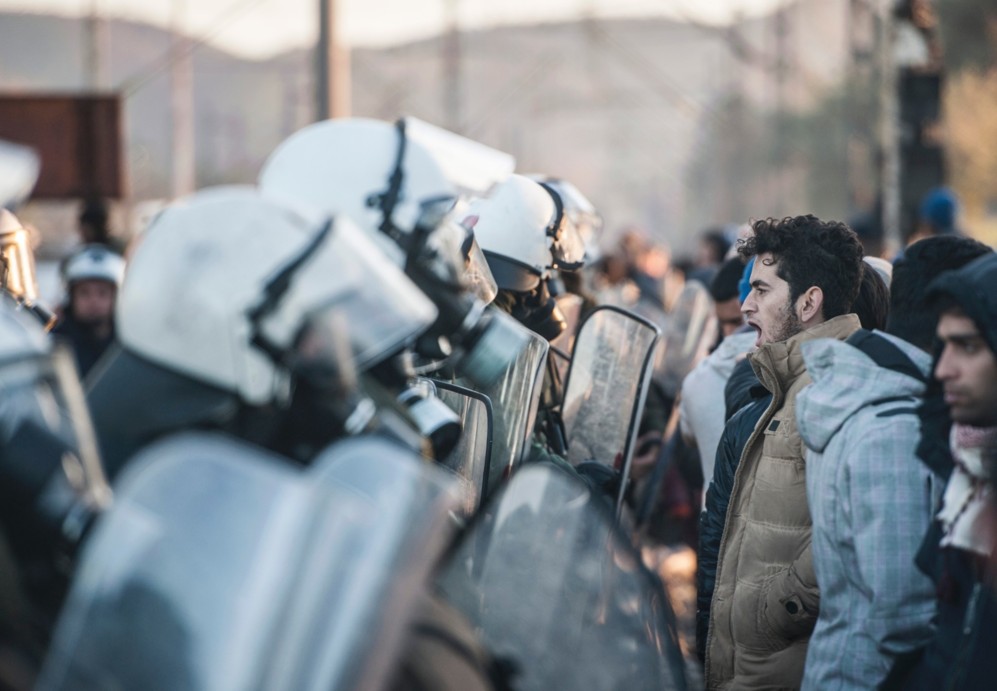Un grupo de refugiadospermanece de pie delante de un cordn policial...