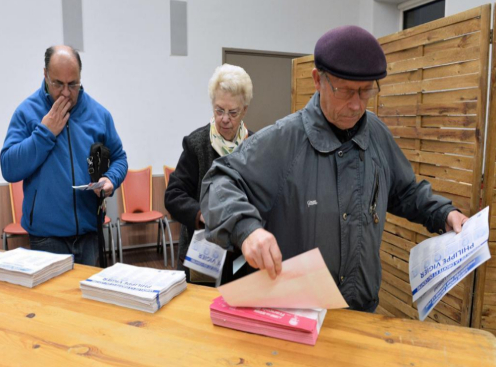 Varios ciudadanos cogen las papeletas en el centro electoral de una...