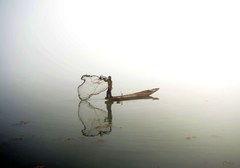 Un pescador de Cachemira lanza la red de su barco en el lago Dal...