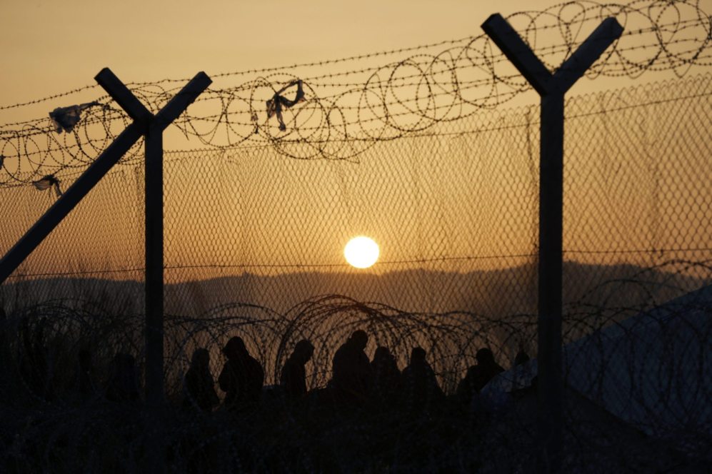 Varios migrantes caminan frente a la puesta de sol tras superar los...