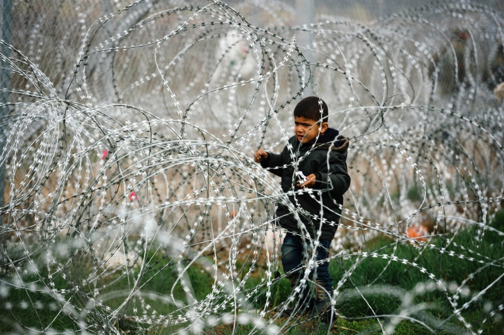 Un nio observa el otro lado de la frontera tras una concertina en la frontera de Grecia con Macedonia.