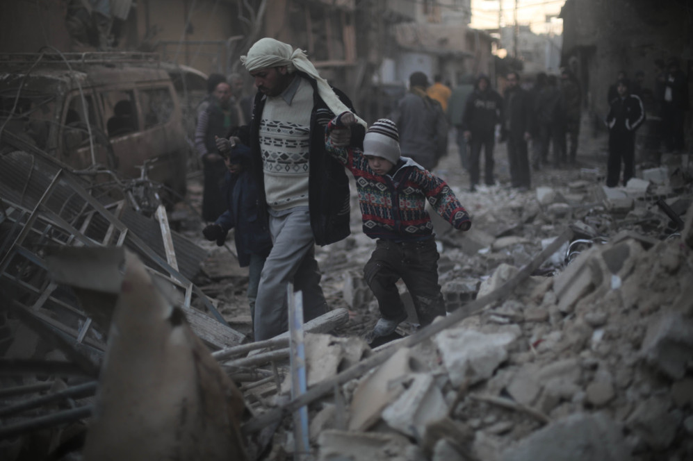 Un hombre ayuda a su hijo a caminar entre los escombros de un edificio...