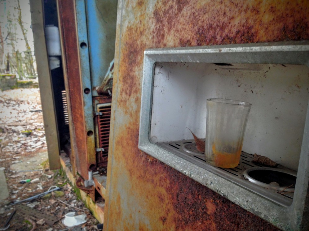 Una mquina de agua con un vaso sucio y oxidado, junto al...
