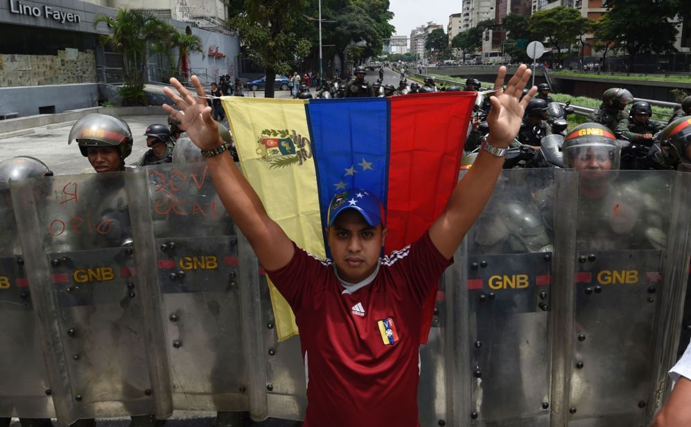 Uno de los manifestantes sostiene la bandera de Venezuela frente al...