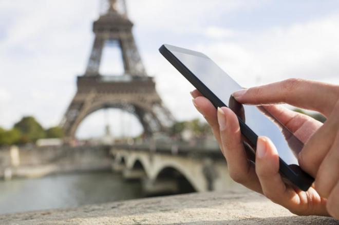 Una persona utiliza su smartphone frente a la Torre Eiffel.