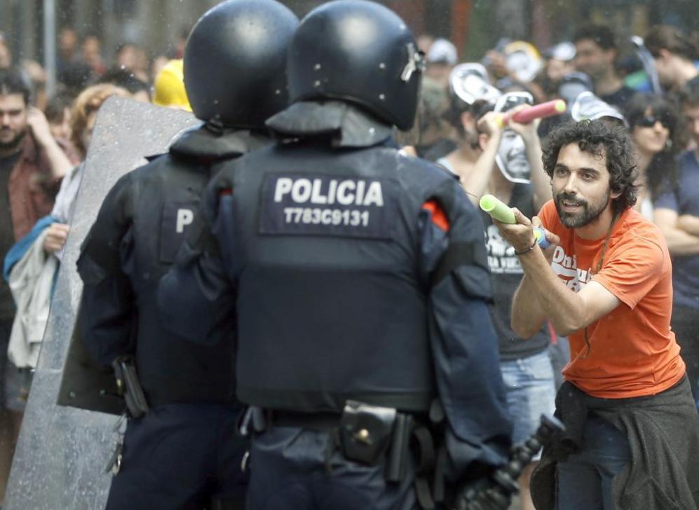 Un manifestante lanza agua a un agente de los Mossos d'Esquadra.