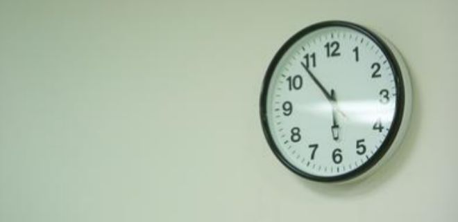 Un reloj a punto de marcar las seis en una oficina.