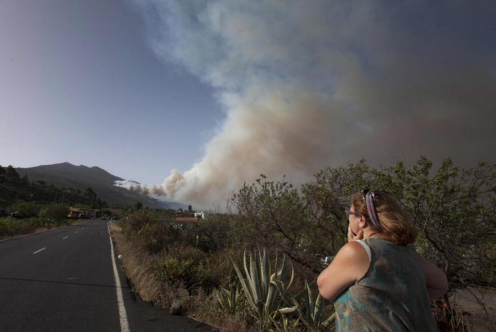 Una mujer presencia los efectos del incendio que cubren de humo el...