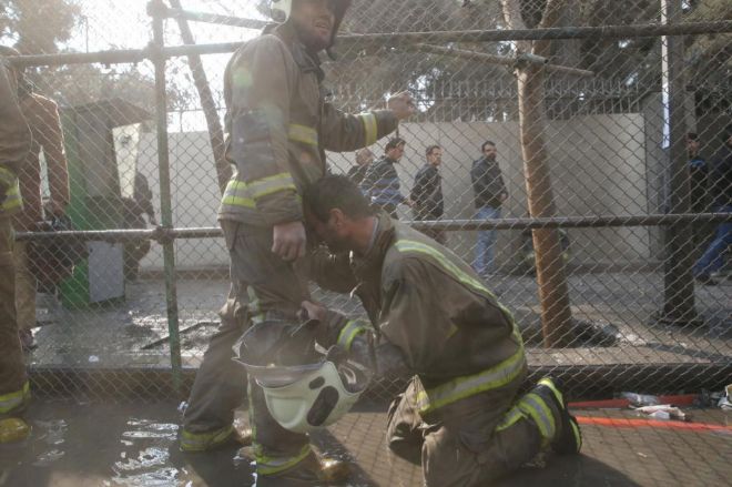 Dos bomberos se consuelan tras el colapso de un edificio en Tehern.