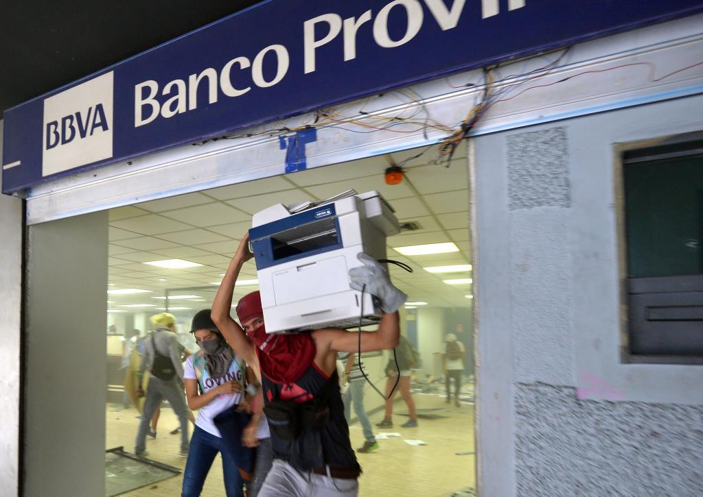 Anti-government demonstrators loot a branch of the Banco Provincial which works inside the administration headquarters of the Supreme Court of Justice after attacking and invading the building as part of protests against President Nicolas Maduro in Caracas, on June 12, 2017. With Venezuelans suffering from high inflation, food shortages and soaring crime rates, plus a deepening corruption scandal, the Venezuelan opposition has mounted near-daily anti-government protests since April 1. The protests have left 66 dead and more than a thousand injured, according to prosecutors. / AFP PHOTO / LUIS ROBAYO