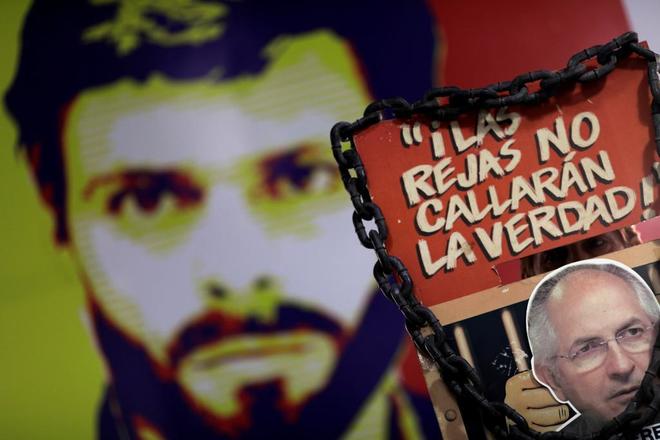 Un hombre sostiene una pancarta con la cara de Antonio Ledezma, al fondo una pared pintada con un retrato de Leopoldo López