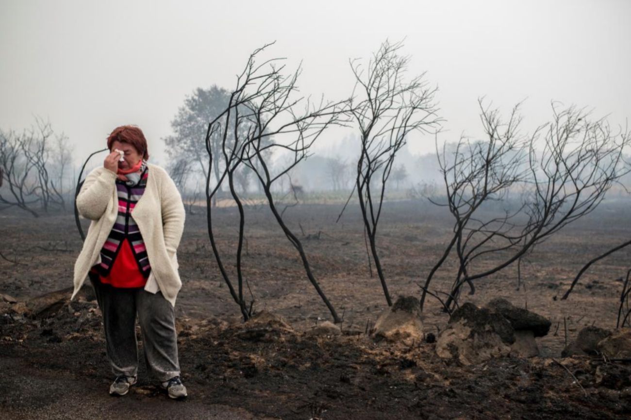 Una mujer llora ante el paisaje calcinado por el fuego, en la zona de...