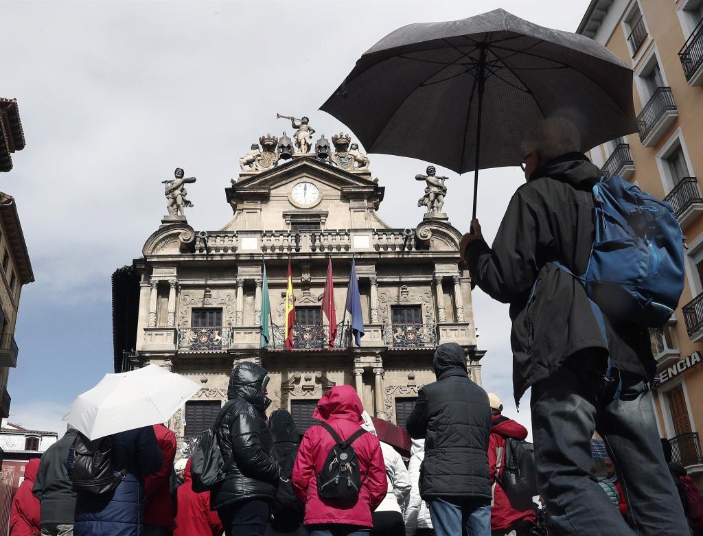 Un grupo de turistas se protegen con sus paraguas de la lluvia junto...
