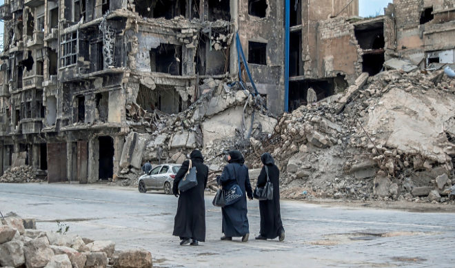 Tres mujeres caminan por una calle de Alepo, entre escombros y edificios derruidos.
