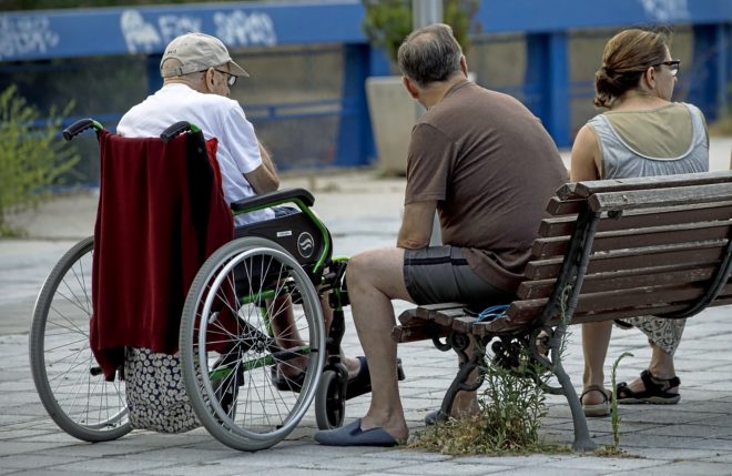 Un anciano en silla de ruedas junto a una residencia en Madrid con dos...