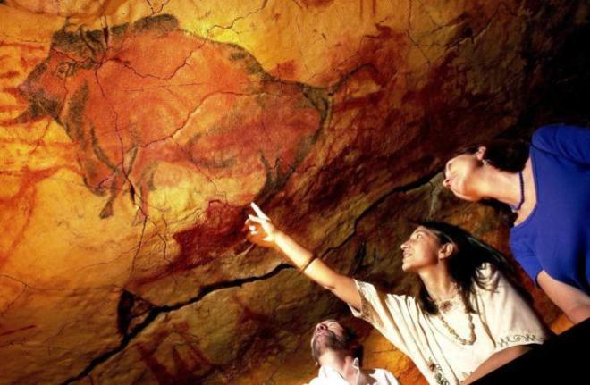 Dos turistas observan las pinturas de la cueva de Altamira.