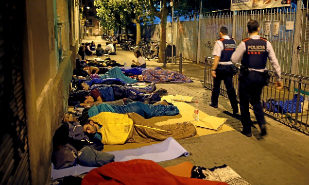 Dos agentes de los Mossos caminan ante personas que duermen a la...