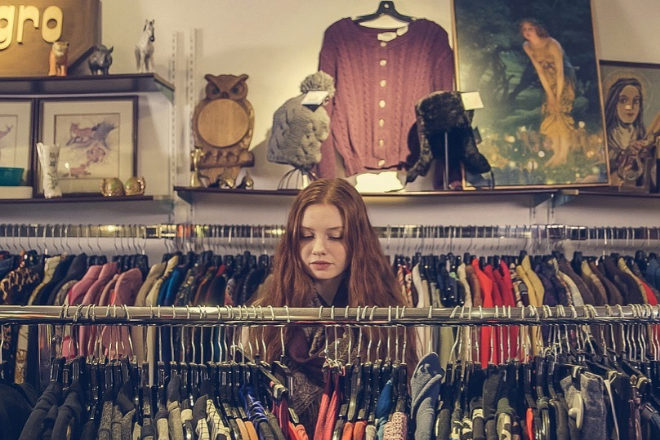 Una chica rebusca entre los percheros de una tienda de moda.