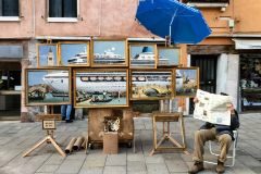 Un hombre, que podra tratarse de Banksy, est sentado al lado del montaje de pinturas 'Venice in oil'
