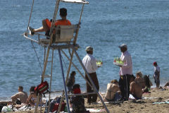 Dos vendedores ambulantes se encuentran frente al socorrista en la playa de la Barceloneta (Barcelona).