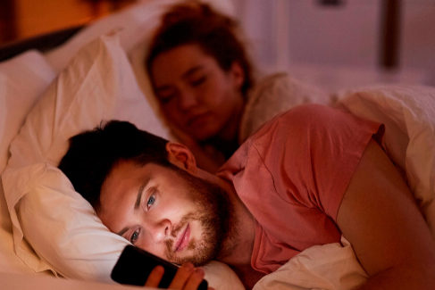 Un hombre mira un telfono mvil mientras su pareja duerme.