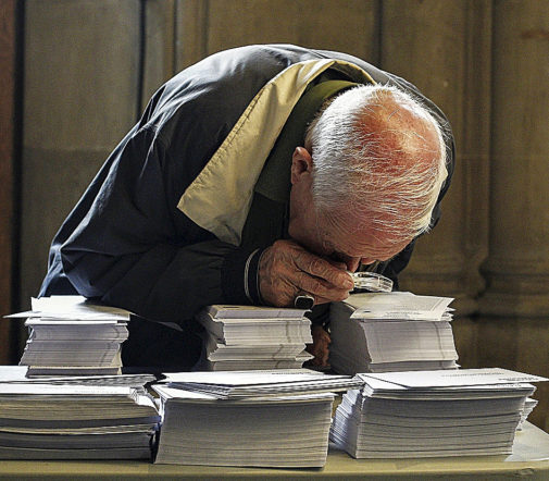 Una persona observa con lupa papeletas electorales.