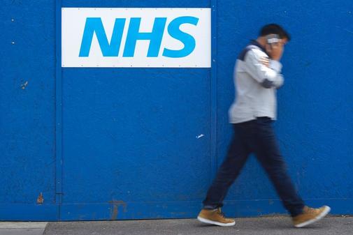 Un hombre pasa junto a un logotipo del Servicio Nacional de Salud...