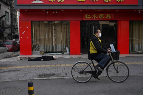 Un hombre pasa en bicicleta ante el cadver de un hombre en Wuhan, en China.